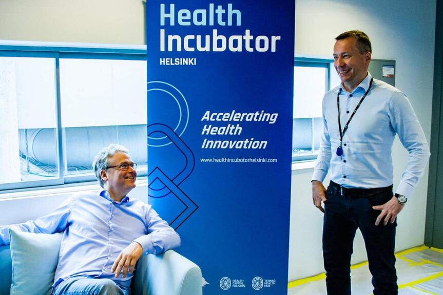 Two men next to the Health Incubator Helsinki roll-up.